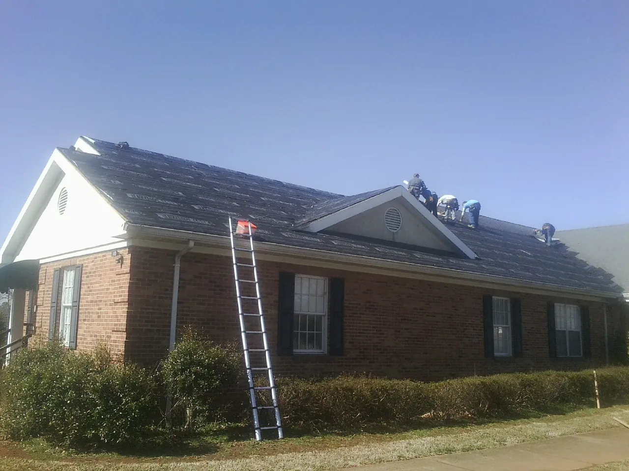 Crew tearing shingles off a brick ranch roof with a ladder set — Metal Roof Repair work by our crew in China